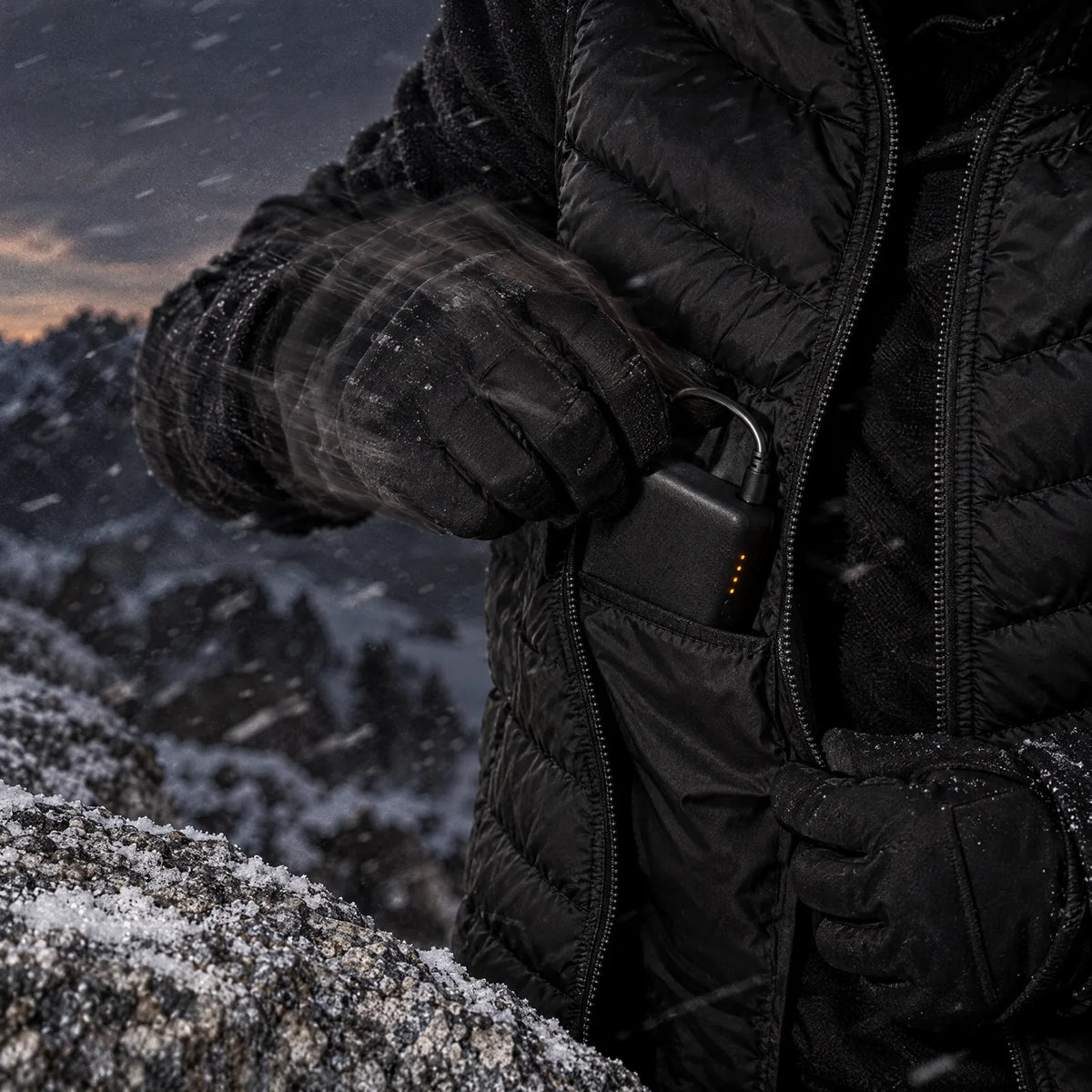 Spare power bank sliding into the inner pocket of a heated vest on a frosted ledge