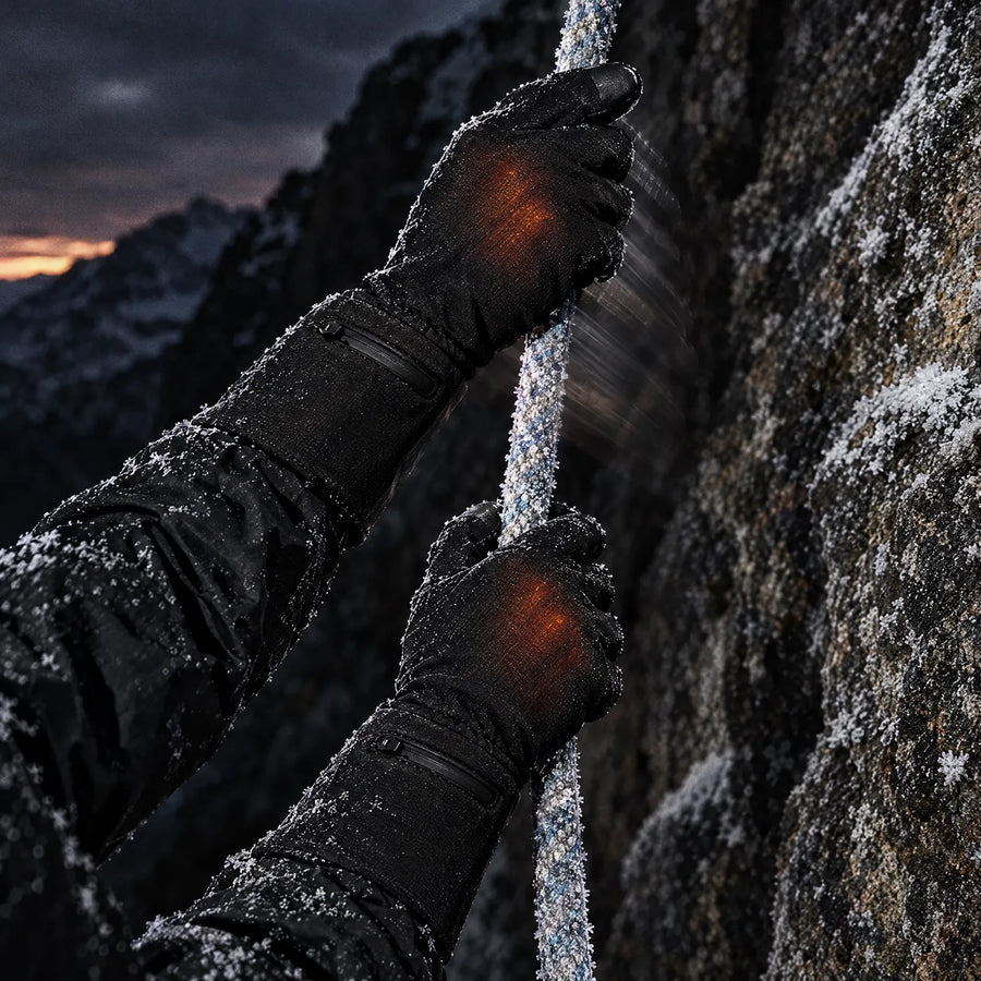 Hands in Belay heated gloves pulling a frosted climbing rope against granite
