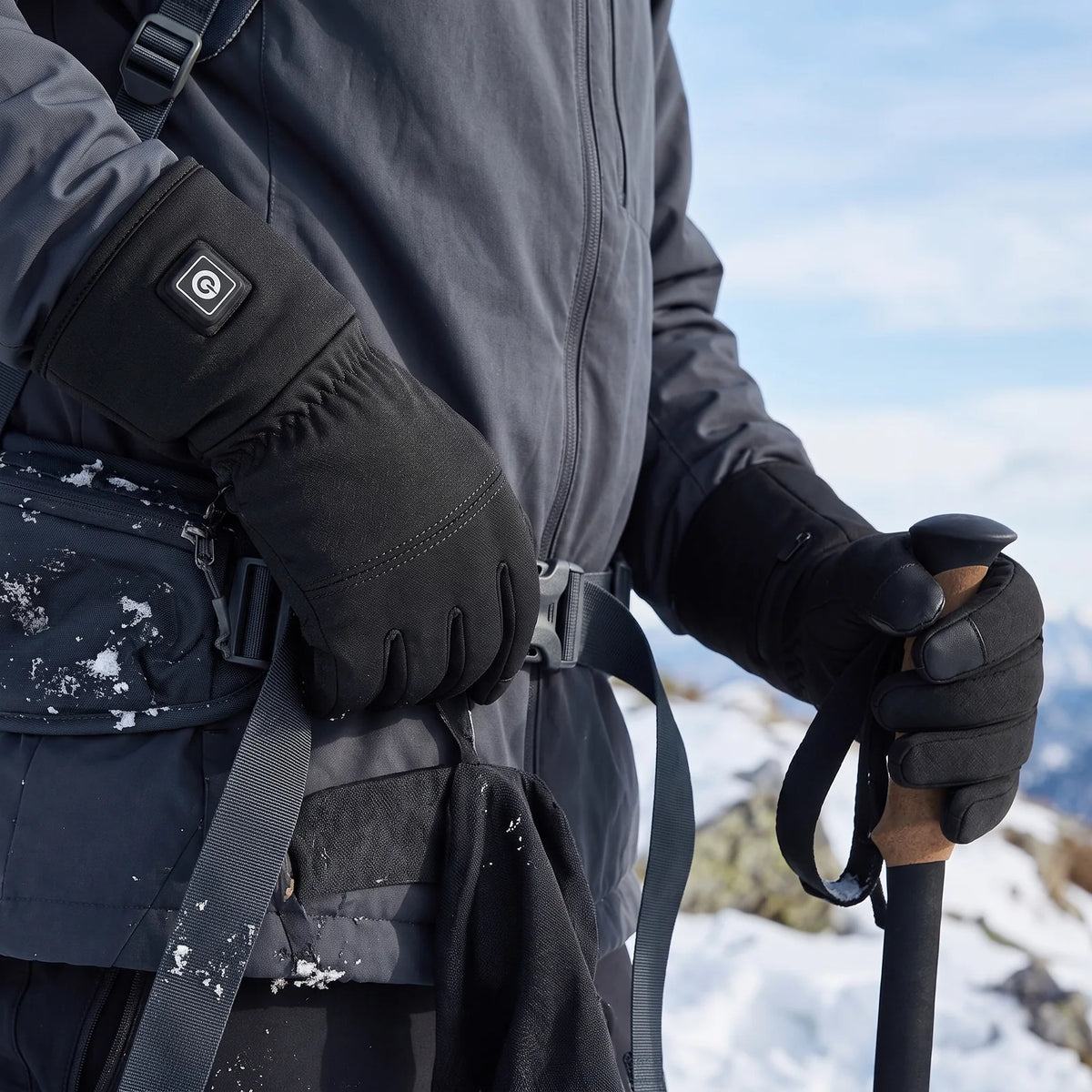 Hiker's hands in Belay heated gloves on a trekking pole and pack buckle