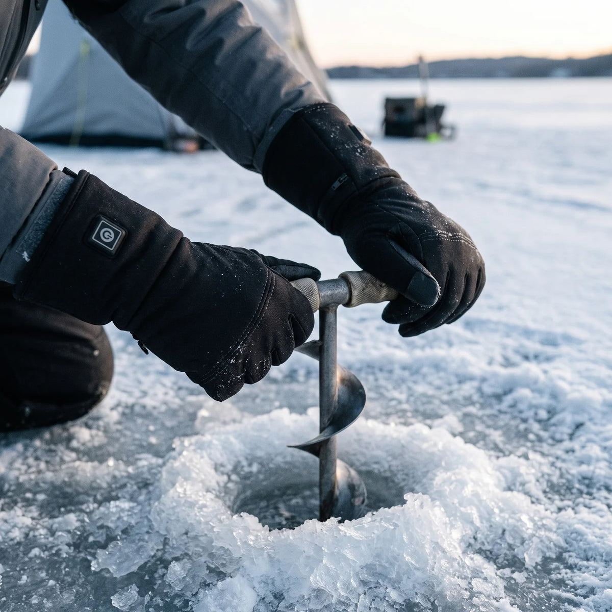 Hands in Belay heated gloves turning an ice auger on a frozen lake