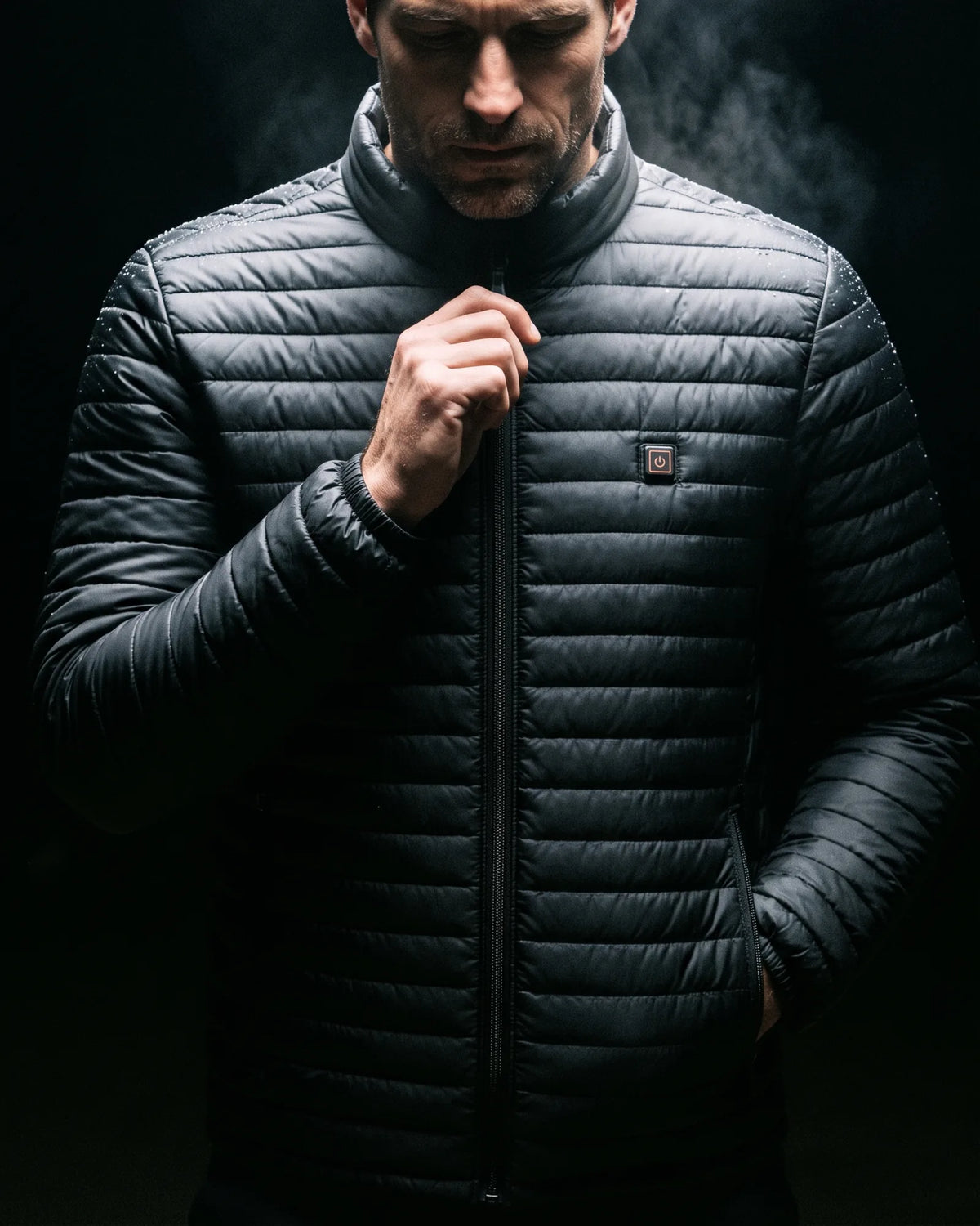 Man zipping up the Basecamp heated jacket in the dark under a single overhead light