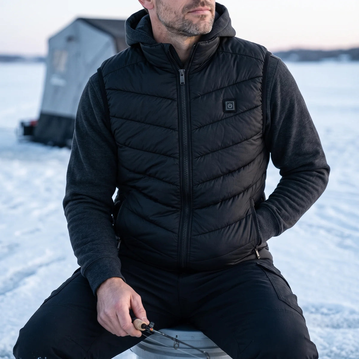 Ice angler on a frozen lake wearing the Treeline men's heated vest over a hoodie