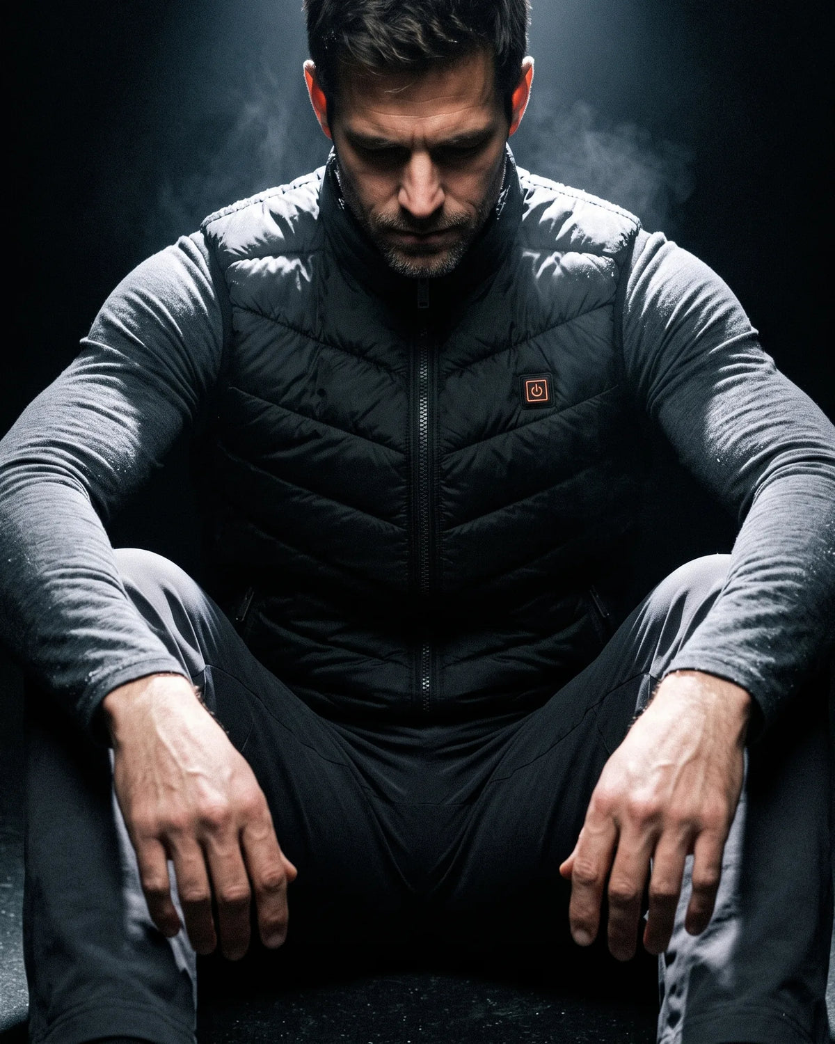 Man in the Treeline heated vest sitting in the dark under a single overhead light