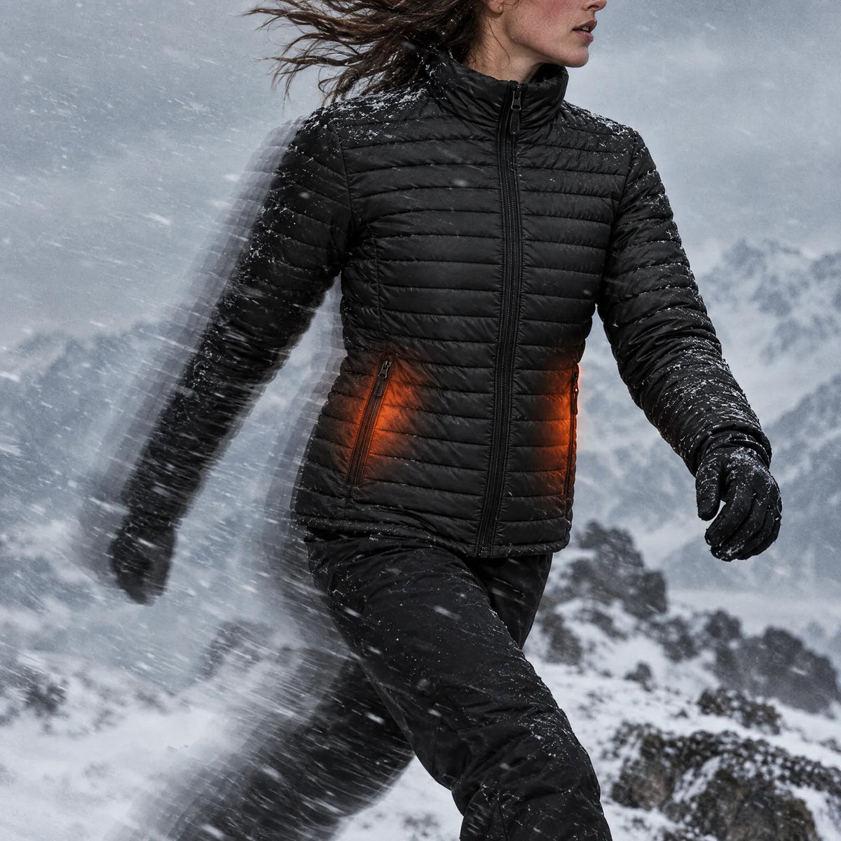 Woman walking a windy snow ridge in the Basecamp women's heated jacket, pocket heat glowing