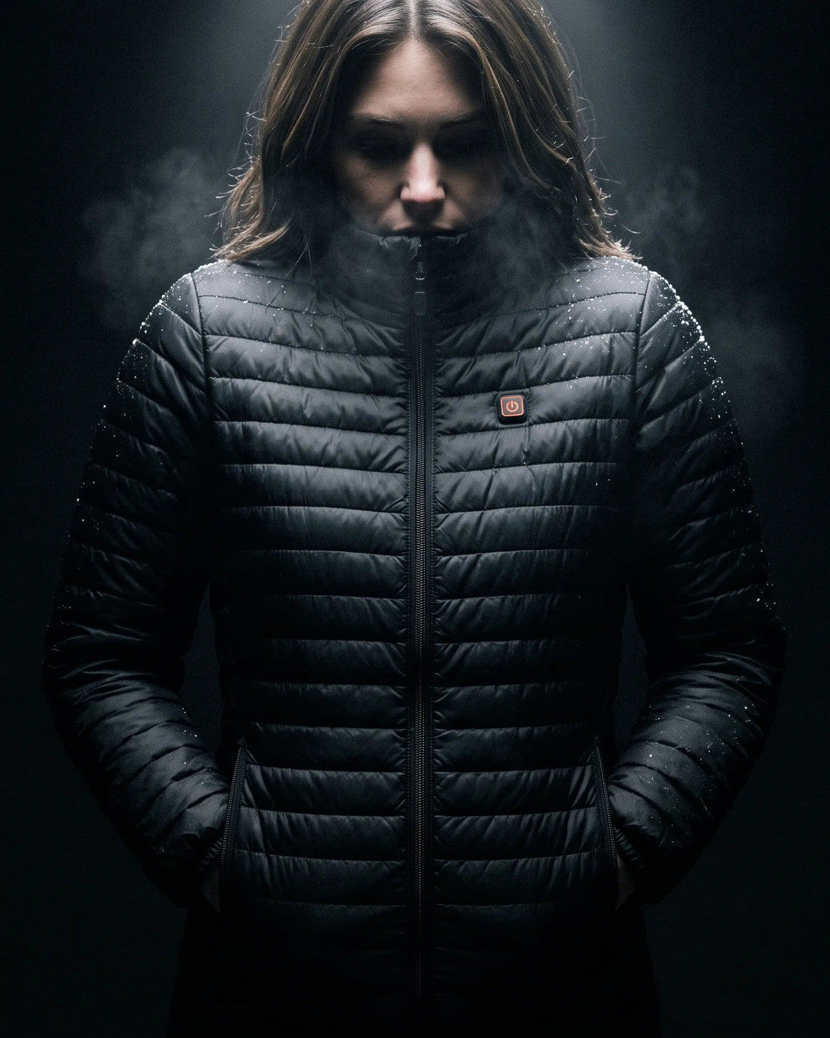 Woman in the Basecamp heated jacket, hands in the heated pockets, lit from above in the dark