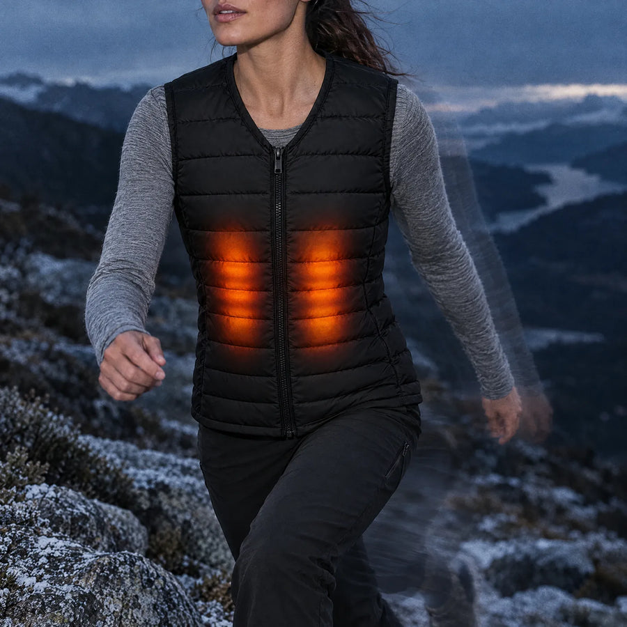 Woman striding up a frosted granite trail in the Ridgeline women's heated vest, front core zones glowing